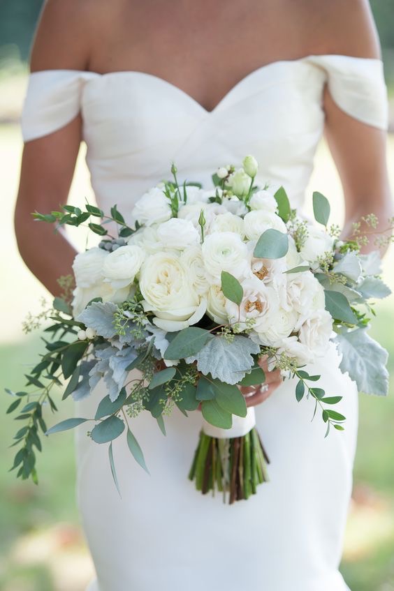 Bride holding bridal bouquet with white roses, ranunculus, lisianthus, seeded eucalyptus, italian ruscus and lambs ear. Soft tones, classy bouquet. White flower